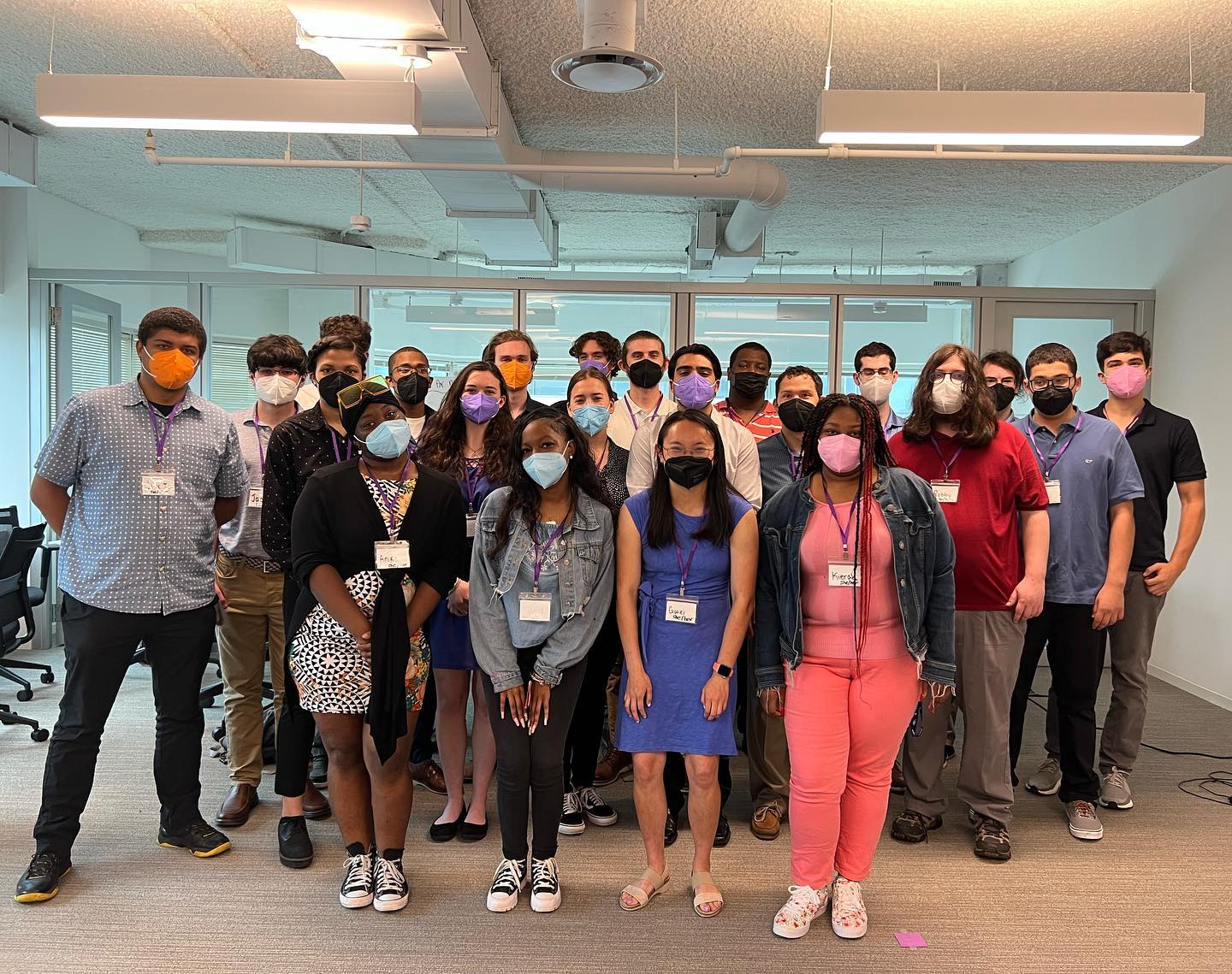 This is a group photo with all of our Summer 2022 interns! Everyone is wearing a face mask and standing close together in our well-lit office space.